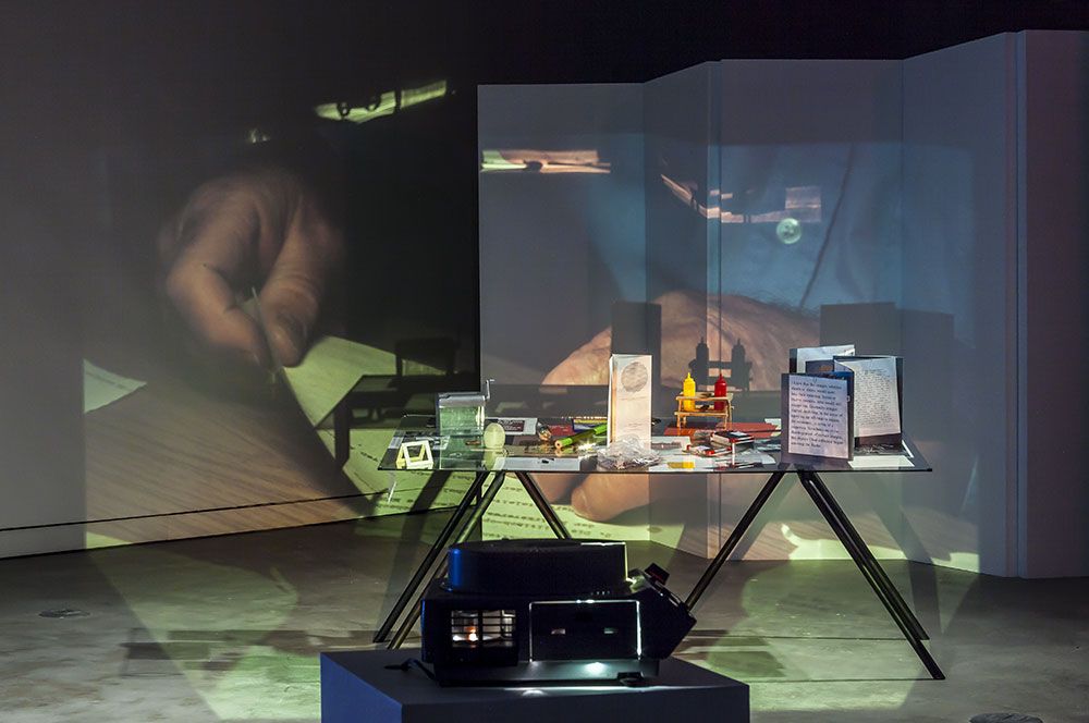 Tris Vonna-Michell, _Finding Chopin: Dans l’Essex_, 2014 (provient de l’œuvre _Finding Chopin_, 2005 – en cours), projection diapositives 35 mm, bande sonore; installation : table, objets et documents divers; vidéo sur moniteur. Crédit : Michel Brunelle.